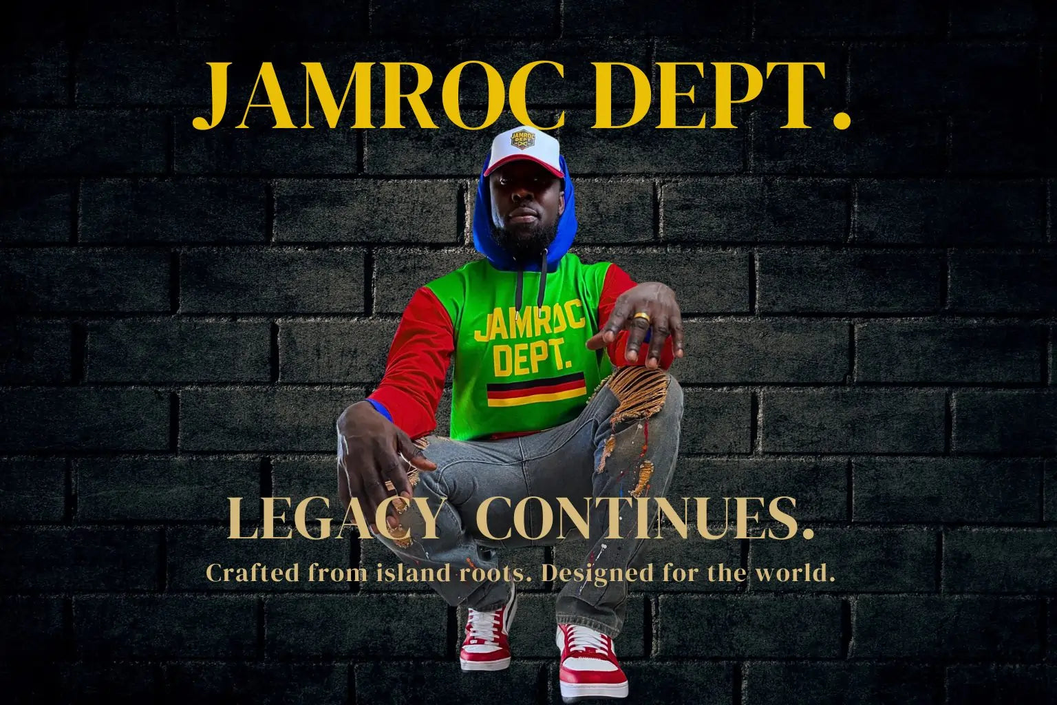 JAMROC DEPT. model wearing a bold red, green, and yellow hoodie with matching cap, crouched against a dark brick wall. The text reads ‘LEGACY CONTINUES. Crafted from island roots. Designed for the world.’ — representing Jamaican streetwear culture with luxury street aesthetic.